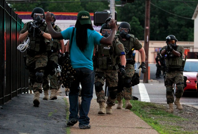 Police wearing riot gear walk toward a man with his hands raised Monday, Aug. 11, 2014, in Ferguson, Mo. Authorities have made several arrests in Ferguson, where crowds have looted and burned stores, vandalized vehicles and taunted police after a vigil for an unarmed black man who was killed by police. (AP Photo/Jeff Roberson)